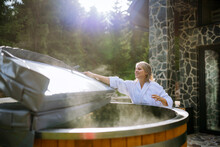 Woman In Bathrobe Opening Lid Of Hot Tub, Checking Temperature, Ready For Home Spa Procedure In Hot Tub Outdoors. Wellness, Body Care, Hygiene Concept.