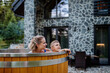 © Halfpoint - Mother with her little son enjoying bathing in wooden barrel hot tub in the terrace of the cottage. Wooden bathtub with a fireplace to burn wood and heat water.