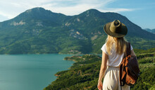 Back View Of Wanderlust Woman With Backpack Looking At Scenic View Of Lake And Mountains From A View Point.