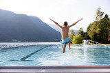 Fototapeta Las - Active teenager boy jumping into an outdoor pool in the Alps. Summer holiday concept
