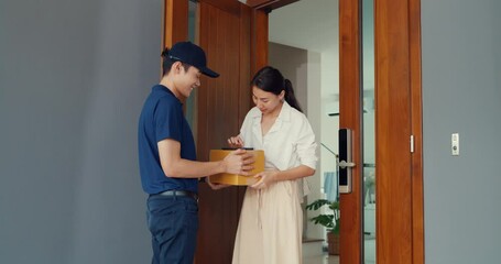 Wall Mural - Young Asian delivery man in blue navy uniform knock door home delivery online shopping box to woman customer in front door and woman sign name accept on smartphone at house. home delivery concept.