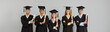 © Studio Romantic - Happy proud diverse mixed race international college or university students in graduate hats and gowns holding paper diplomas and smiling at camera standing on gray background at graduation event