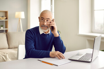 Wall Mural - Serious mature businessman work on laptop at home office talk on cellphone call with business client. Focused middle-aged man boss or CEO use computer have smartphone communication online.