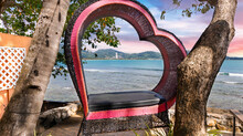 Magnificent  View Of Patong Beach Through A Love Heart Lounge Chair. Multi Coloured Sky At Sunset And Sunrise. Lush Green Mountains And Turquoise Blue Waters Of The Beach