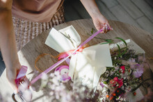 a woman florist ties a pink ribbon bouquet wrapped in paper. The bouquet lies on a round wooden table. Top view