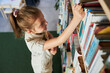 © Przemek Klos - School girl looking at bookshelf in school library. Smart girl selecting literature for reading. Books on shelves in bookstore. Learning from books. Back to school. School education