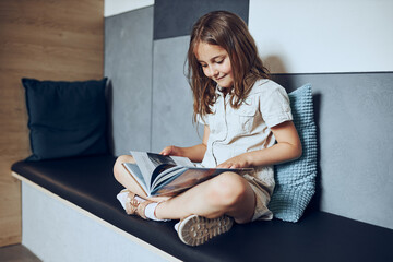 Wall Mural - Schoolgirl reading book in school library. Primary school pupil is involved in book. Child doing homework. Smart girl learning from book. Benefits of everyday reading