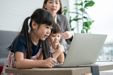 Asian mother with her two grandchildren having fun and playing education games online with a digital computer laptop at home in the living room. Concept of online education and caring from parents.