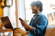 © Drobot Dean - Young smiling handsome indian curly man looking phone while working