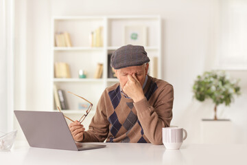 Sticker - Elderly man having a headache and holding a document and sitting in front of a laptop computer