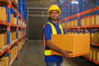 © tonefotografia - Young mixed race male worker wearing helmet lifting cardboard box in warehouse, machinery and Logistics concept.