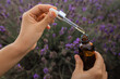 Dropper with lavender essential oil over a bottle in a blooming field, close-up.