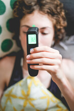 Teenager Lying In Bed Taking His Temperature With A Digital Thermometer