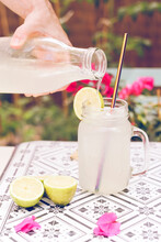 Close-up Of A Woman Pouring A Glass Of Frozen Lemonade On A Garden Table