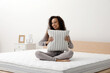 © New Africa - Happy young African American woman hugging pillow on bed with comfortable mattress at home