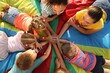 © New Africa - Group of children with teachers holding hands together on rainbow playground parachute, top view. Summer camp activity