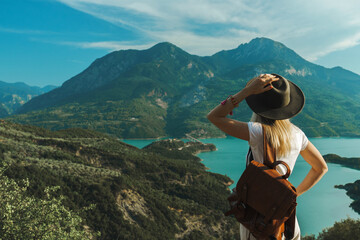 back view of wanderlust woman with backpack looking at scenic view of lake and mountains from a view