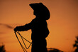 Western culture shows silhouette of child cowboy practicing in sunset with rope for rodeo roping lifestyle on ranch.