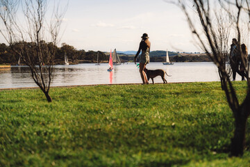 woman walking dog near lake with sailing