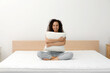 © New Africa - Happy young African American woman hugging pillow on bed with comfortable mattress at home