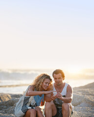 Wall Mural - Young couple using smartphone on beach at sunset