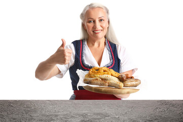 Poster - Mature Oktoberfest waitress holding plate with snacks and showing thumb-up at table on white background