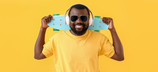 Wall Mural - Handsome African-American man with headphones and skateboard on yellow background