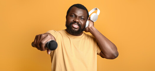 Canvas Print - Male African-American singer with headphones and microphone on orange background