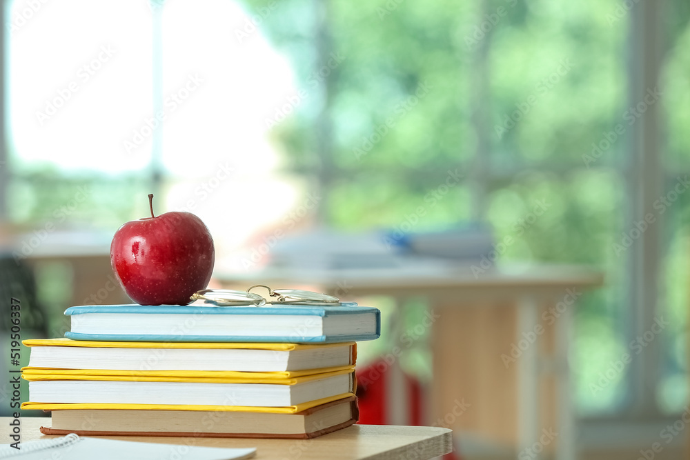 Apple with school books and eyeglasses on table in classroom