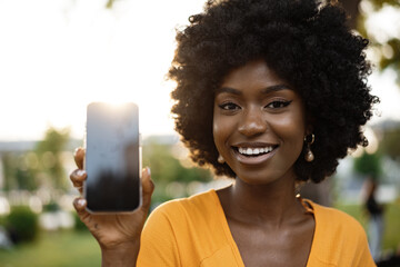 Portrait of a smiling young african woman holding blank screen mobile phone standing in the street