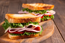 Close-up Of Two Toasted Sandwiches With Fresh Ham, Cheese And Vegetables On Background. Club Sandwich And Take-away Concept. Fast Food. 