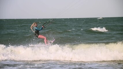 Wall Mural - Young adult caucasian woman in good shape enjoys riding a kiteboard for surfing, doing extreme tricks on a bright sunny windy day