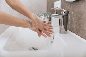 Wall Mural - Washing hands under the flowing water tap. Hygiene concept hand detail. Washing hands rubbing with soap for corona virus prevention, hygiene to stop spreading corona virus in or public wash room.