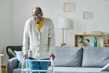 Portrait Of African Senior Man With Disability Smiling At Camera While Learning To Walk With Walker In The Room