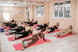© svetograph - A group of six athletic women doing pilates or yoga on pink mats in front of a window in a beige loft studio interior. Teamwork, good mood and healthy lifestyle concept.