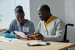 © AnnaStills - African senior man learning to pay online with credit card using digital tablet together with caregiver at table