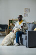© AnnaStills - African senior man in dark glasses with stick sitting on sofa with guide dog in the living room