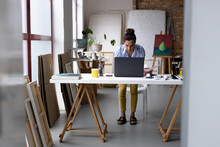 Image Of Biracial Female Artist Using Laptop And Doing Business Work In Studio
