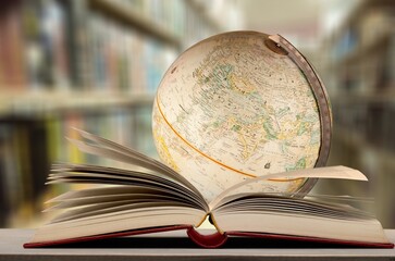 Old globe lying on an open book against the background of bookshelves in a library. Science, education, travel. Education history and geography team.