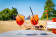 Two glasses of orange spritz aperol drink cocktail on table outdoors with sea and trees view blurred background.