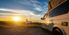 Surfer Girl Sitting Near Her Mini Van And Looking On The Ocean At Summer Sunset  With A Surfboard On Her Side