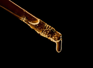 close-up of a serum oil pipette with a falling drop on a dark background