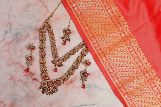 Indian red-pink (coral color) sari fabric and jewelry on a light background. Wedding dress.