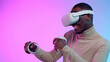 African-American man play video game in ve helmet and controllers isolated over neon background
