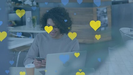 Poster - Animation of yellow and blue heart icons over biracial man using smartphone at a cafe