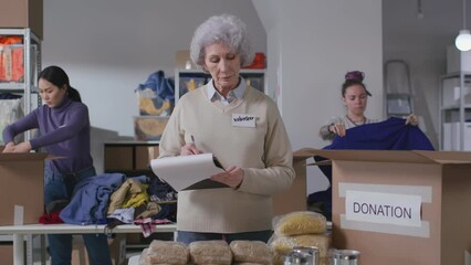 Wall Mural - Senior woman with clipboard pack food for refugees in donation center