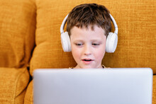 Boy sitting on a sofa with headphones on his head and using the laptop