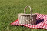 Fototapeta  - Picnic basket with checkered tablecloth on green grass outdoors, space for text
