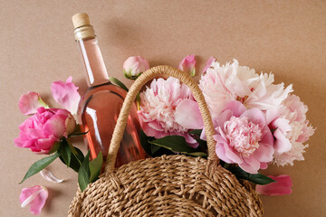 Canvas Print - Wicker bag with bottle of rose wine and beautiful pink peonies on brown background, top view