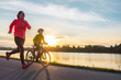 Happy mother and son go in sports outdoors. Boy rides bike in helmets, mom runs on sunny day. Silhouette family at sunset. Fresh air. Health care, authenticity, sense of balance and calmness
